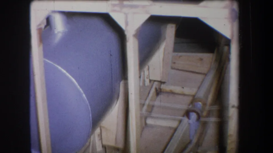 1965 Yucaipa 8mm still showing the blue drum closer in frame, with vertical posts and a wooden support assembly beside it.