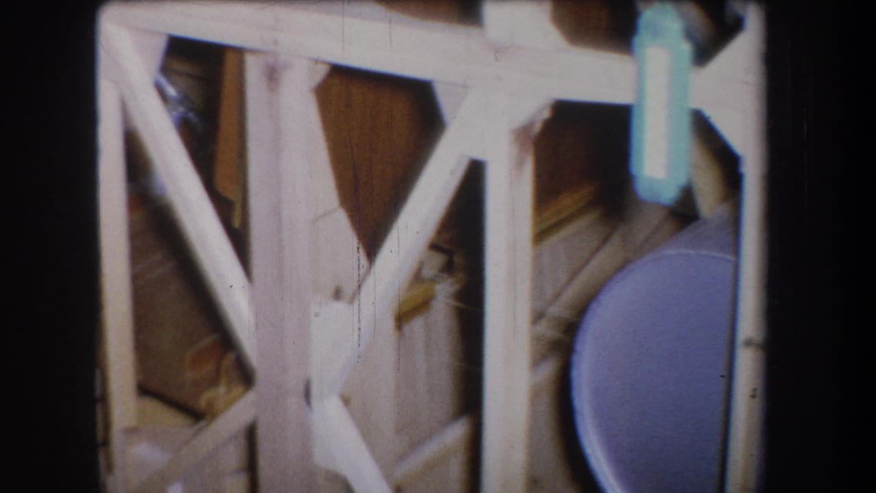 White cross-braced wooden framework with part of the blue tank at right.