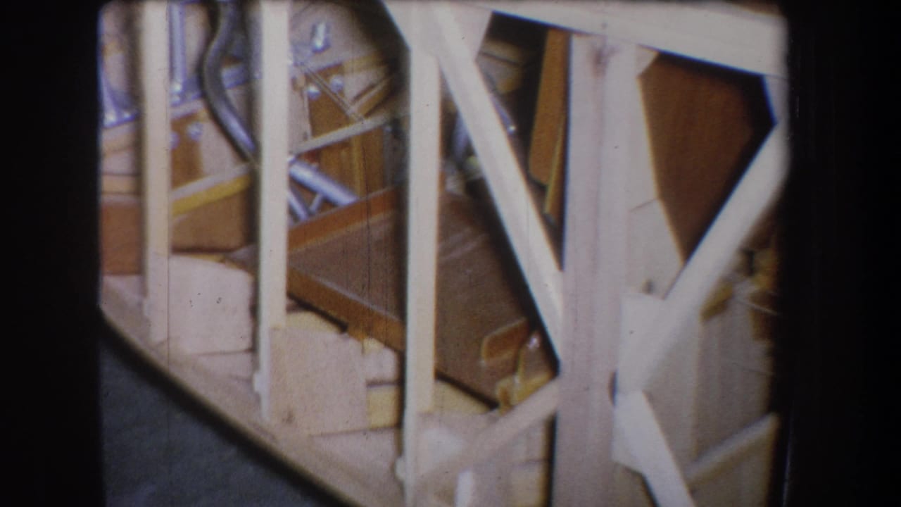 1965 Yucaipa home-movie frame showing white wooden rails, exposed framing, and a partially visible workshop area.
