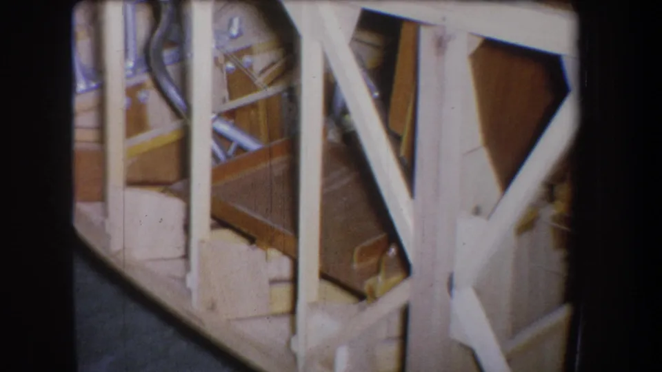 1965 Yucaipa home-movie frame showing white wooden rails, exposed framing, and a partially visible workshop area.