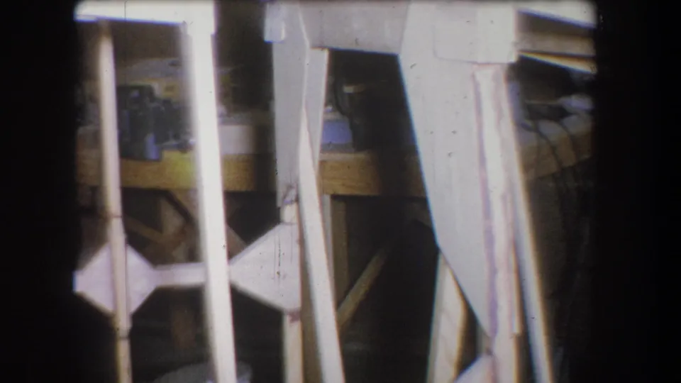 Handheld 8mm frame from a Yucaipa garage, with white supports, a bench edge, and shadowed storage or work areas.