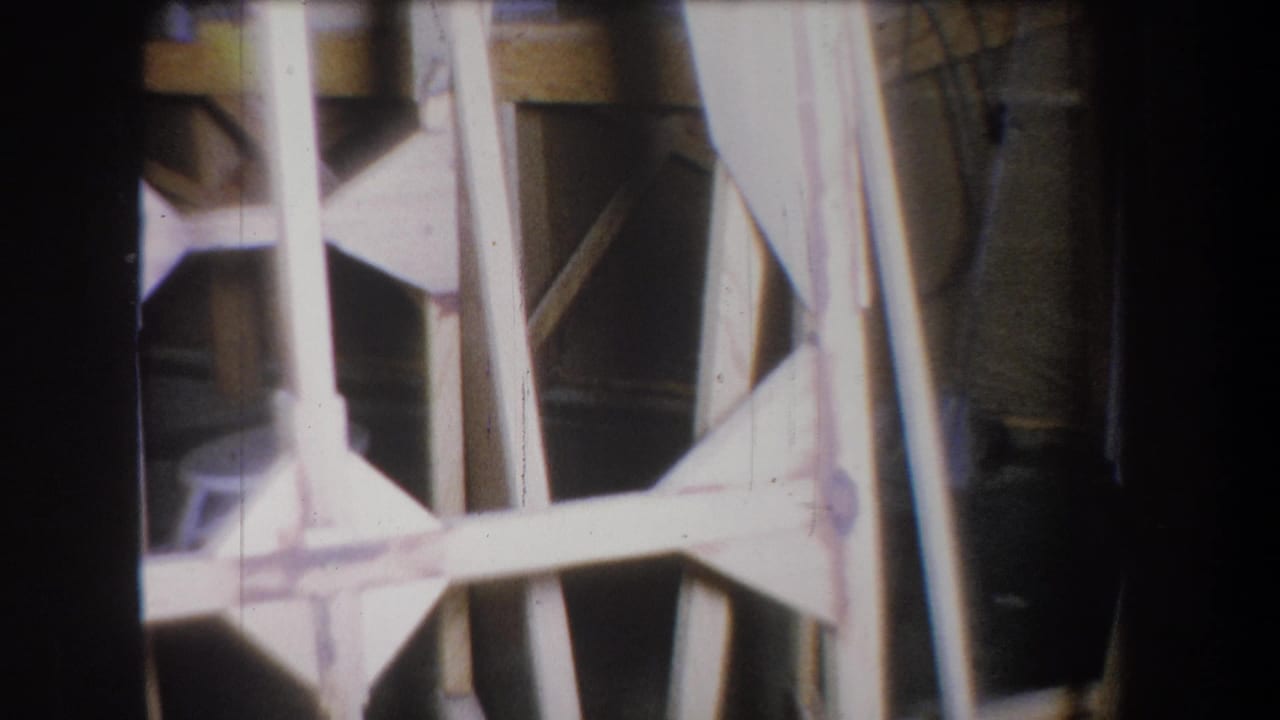 1965 Yucaipa 8mm frame showing a tan wooden structure with vertical posts and cross braces in dim interior light.