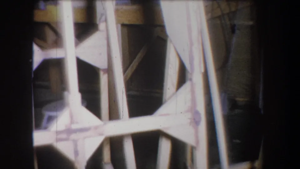 1965 Yucaipa 8mm frame showing a tan wooden structure with vertical posts and cross braces in dim interior light.