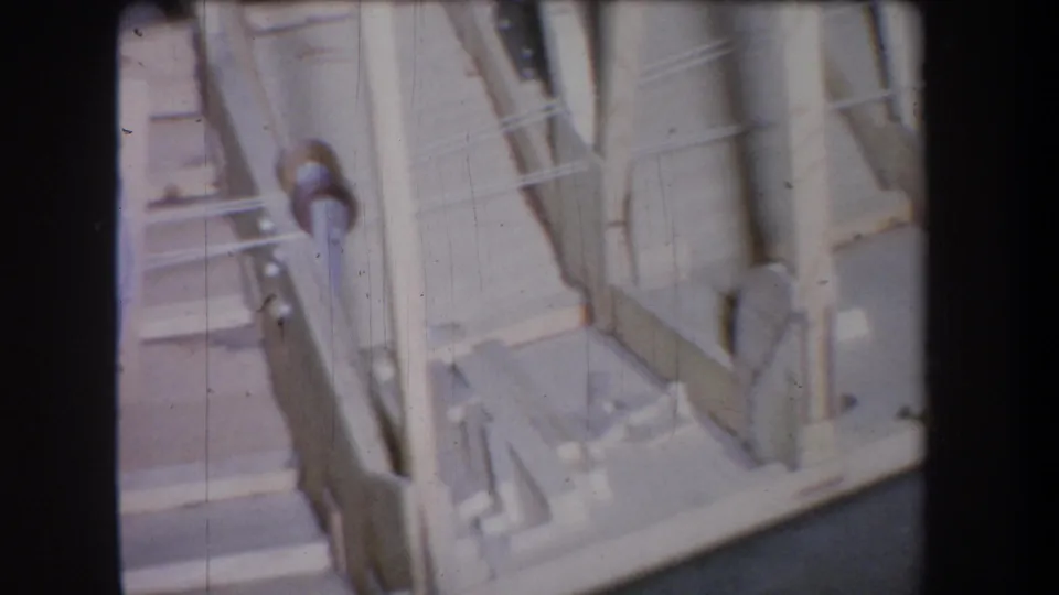 Final 1965 Yucaipa 8mm frame showing pale wood supports, diagonal braces, and shadowed openings in the storage area.