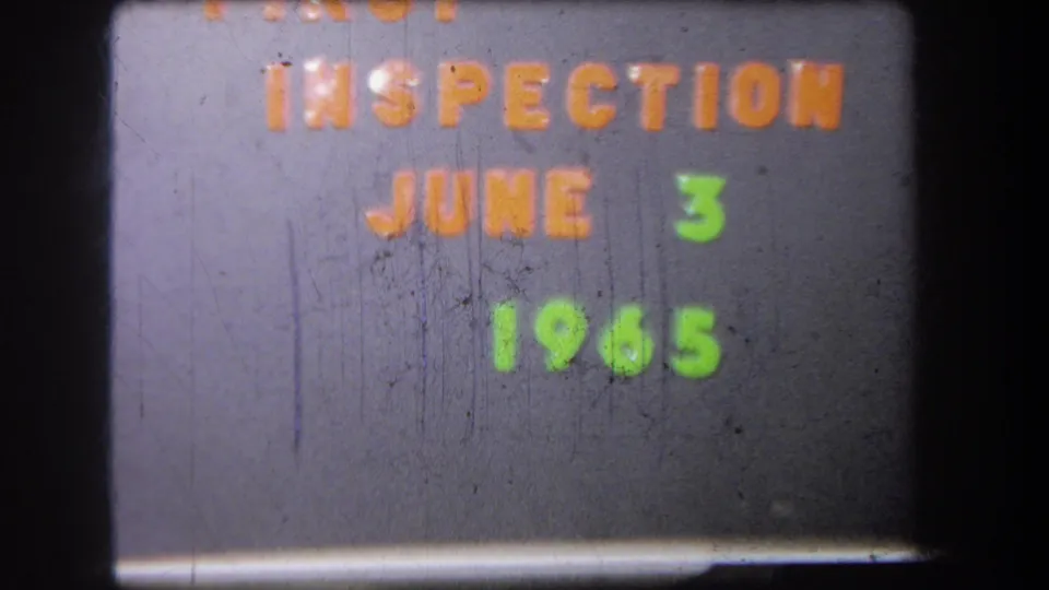 Another 8mm frame of the inspection announcement card, showing orange and green lettering with visible scratches and soft exposure.