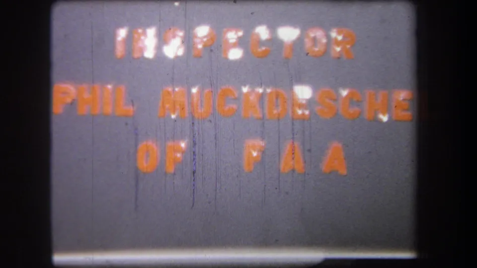 1965 title card frame showing orange text that appears to read inspector Phil Muckdesche of FAA, with some letters softened by blur.