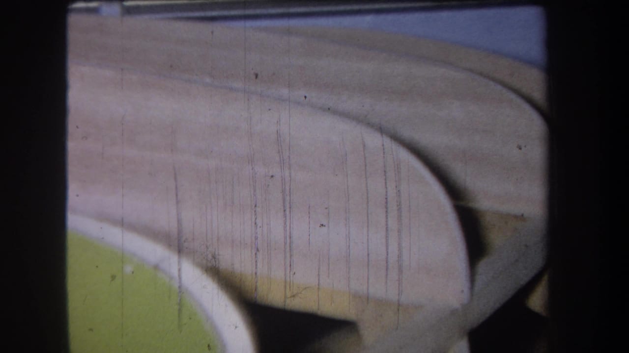 1965 Yucaipa-area 8mm frame showing a close-up of a curved beige structure over green paint, marked by film scratches and gate edges.