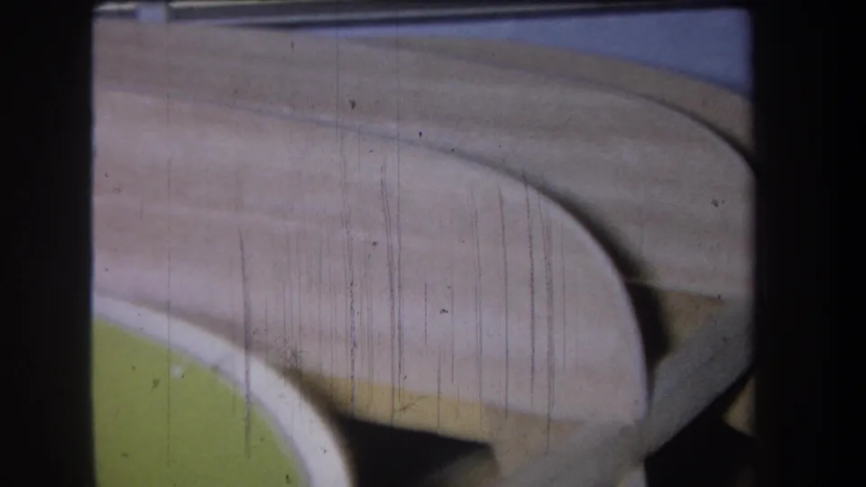 1965 Yucaipa-area 8mm frame showing a close-up of a curved beige structure over green paint, marked by film scratches and gate edges.