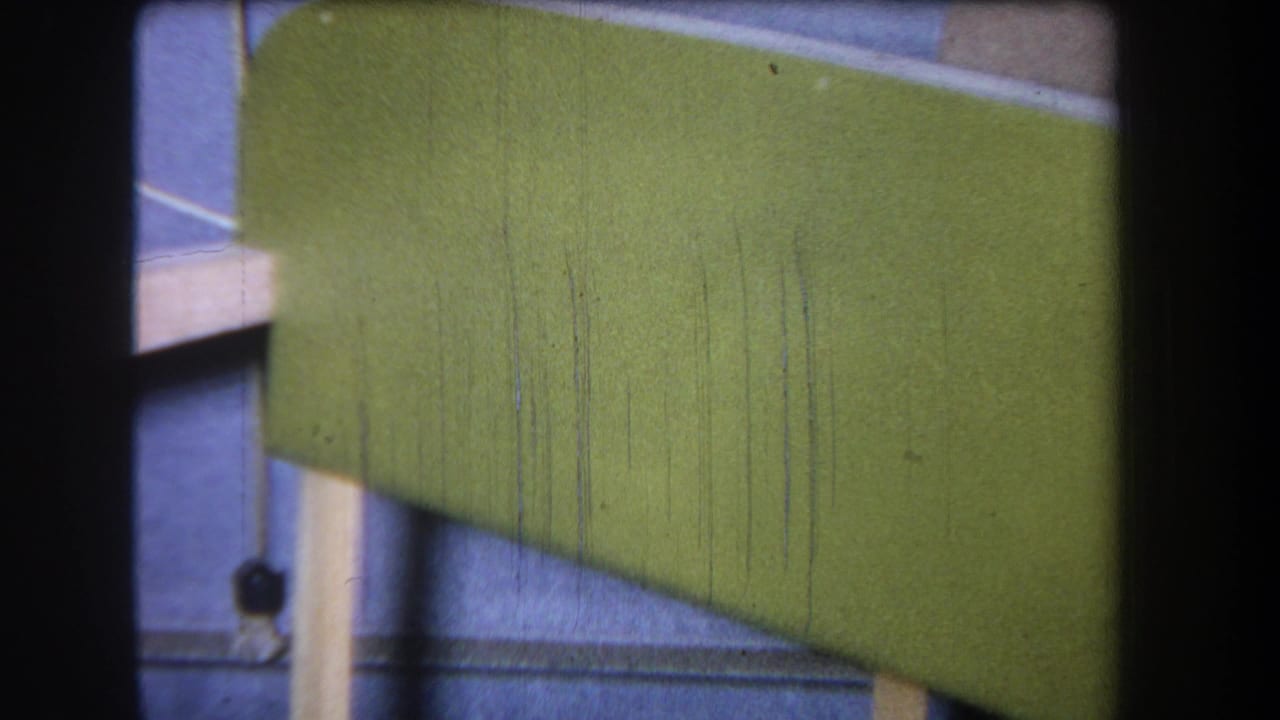 1965 8mm frame from Yucaipa showing a green painted wooden tray or stacked wooden object with pale supports and visible film wear.