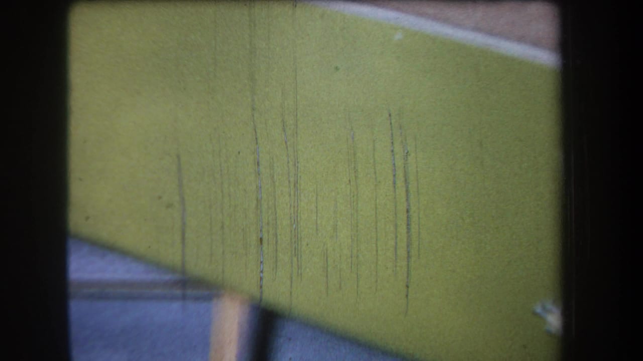 Close 1965 home-movie view of a green wooden tray side in Yucaipa, with pale edging, soft focus, grain, and scratches.