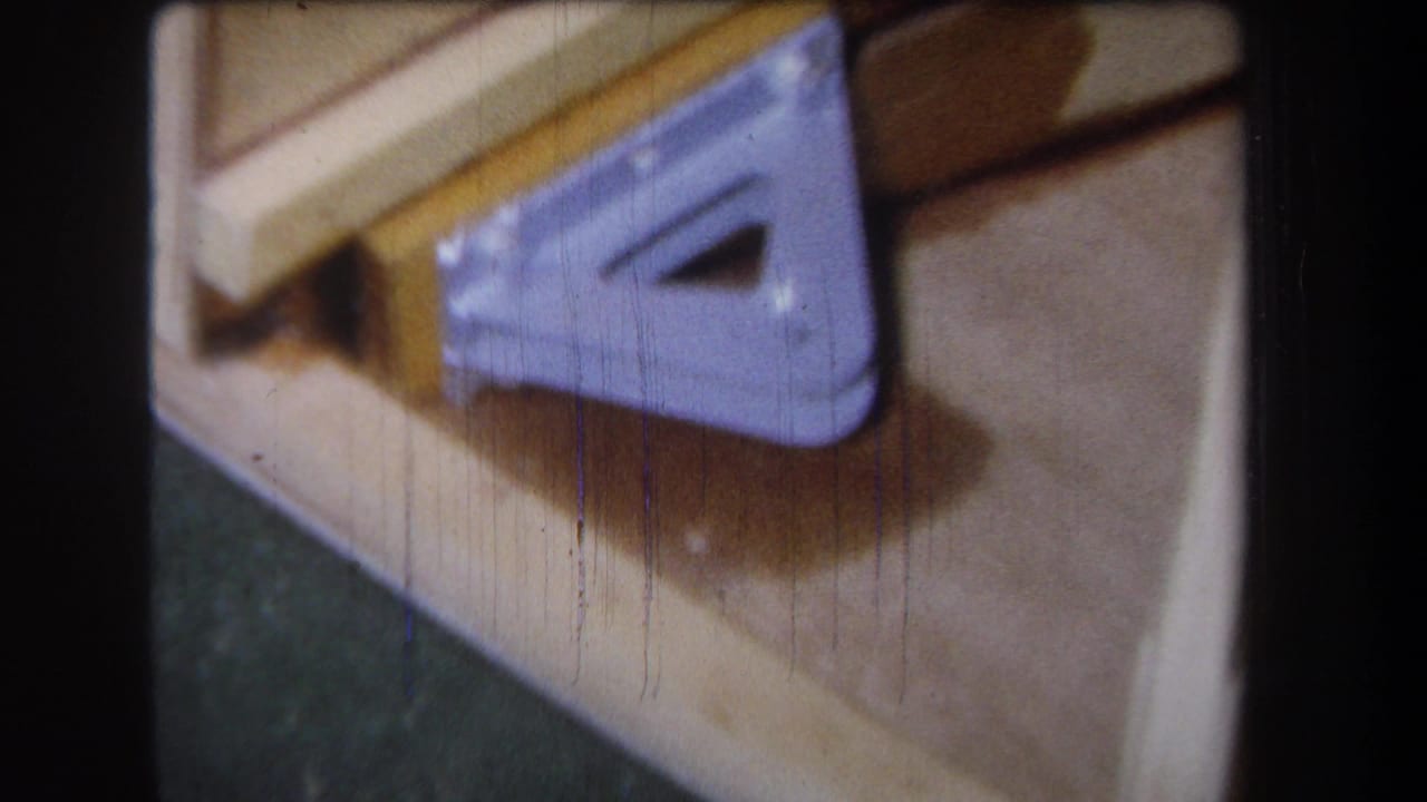 1965 Yucaipa 8mm frame showing light wood boards and a purple triangular metal bracket in soft handheld close-up.