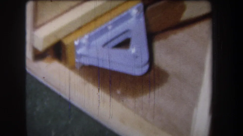 1965 Yucaipa 8mm frame showing light wood boards and a purple triangular metal bracket in soft handheld close-up.