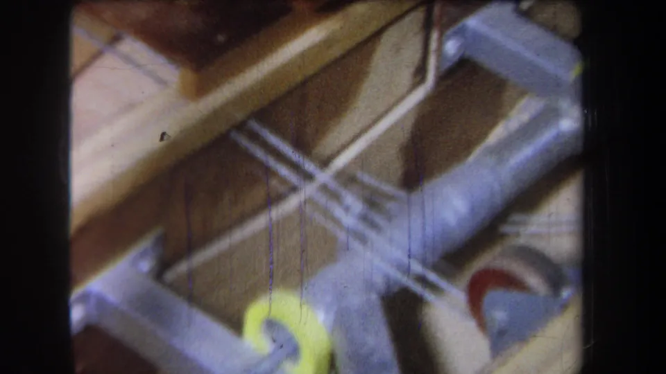 1965 home-movie frame from Volmer Yucaipa showing metal ducting, wood framing, and a yellow wheel-like component in an attic space.