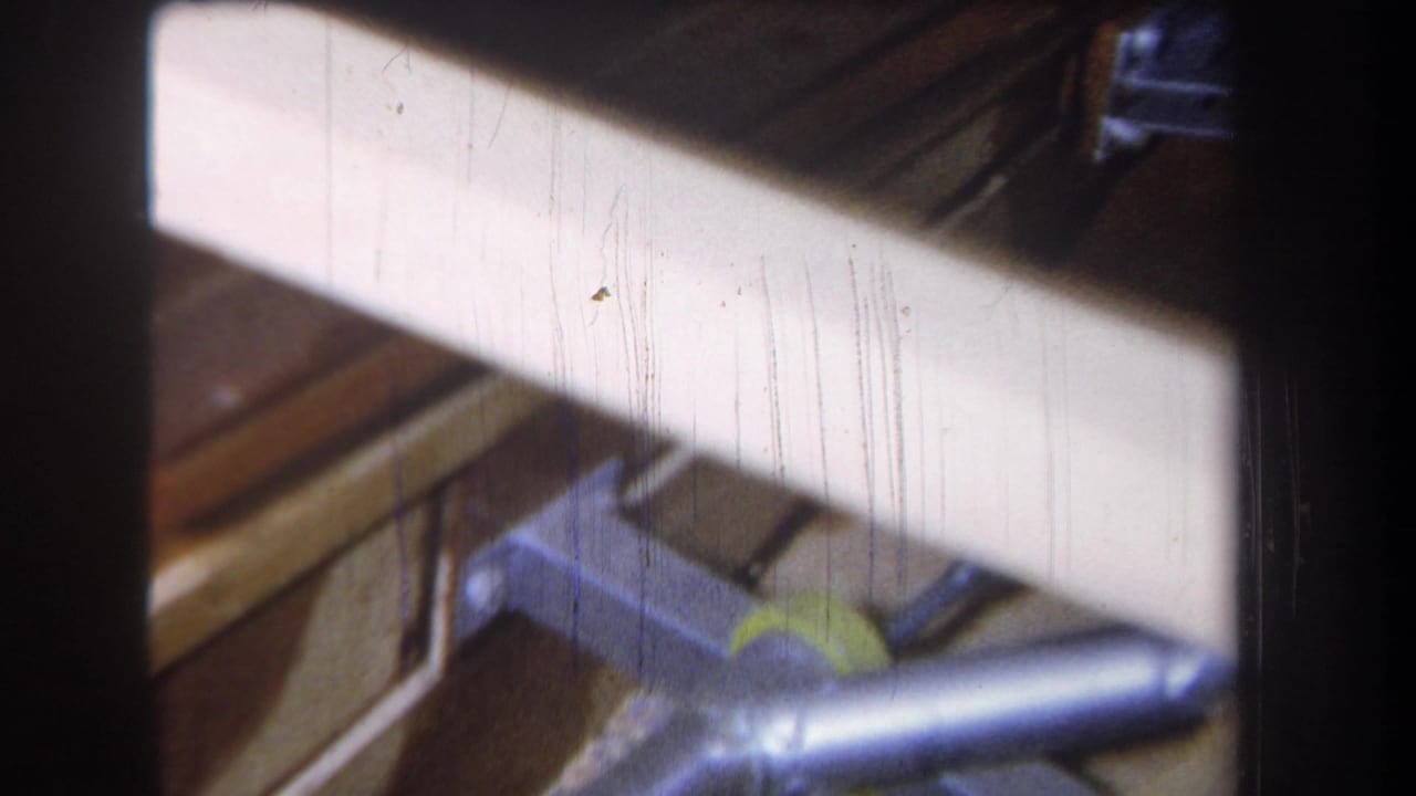 Galvanized duct run crossing wood framing with a bright attic surface behind it.