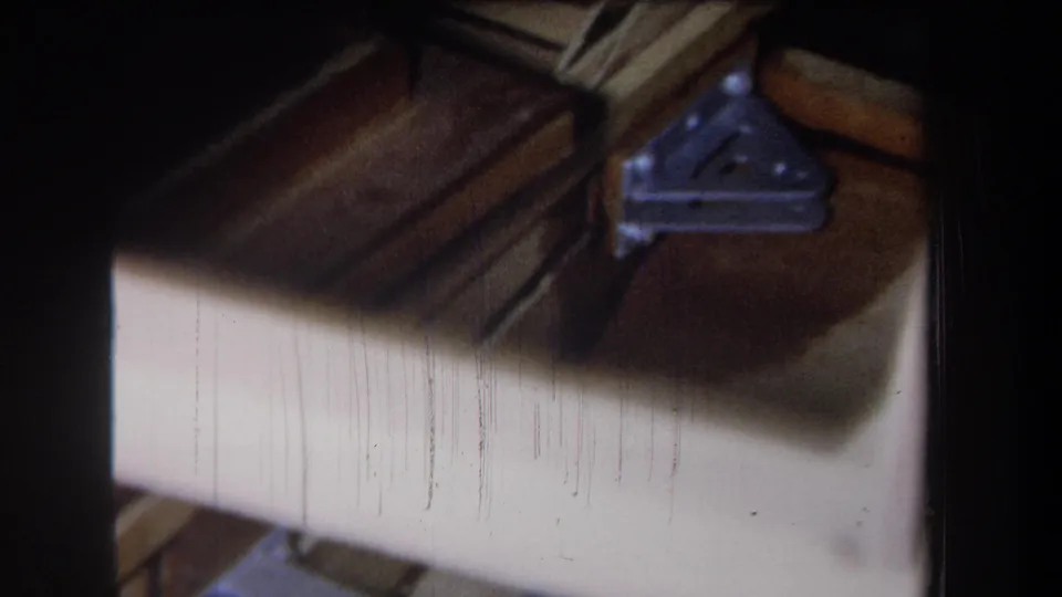 Home-movie attic frame showing wood beams, a triangular metal bracket, and pale sheathing or surface material in the Yucaipa-area footage.