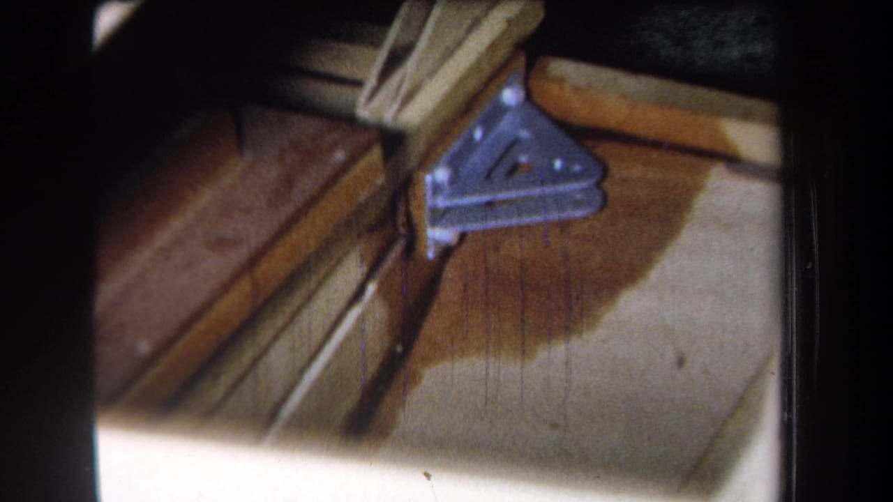 1965 Yucaipa-area 8mm frame showing a blue-gray triangular brace fixed to exposed lumber near a dark damp-looking stain.