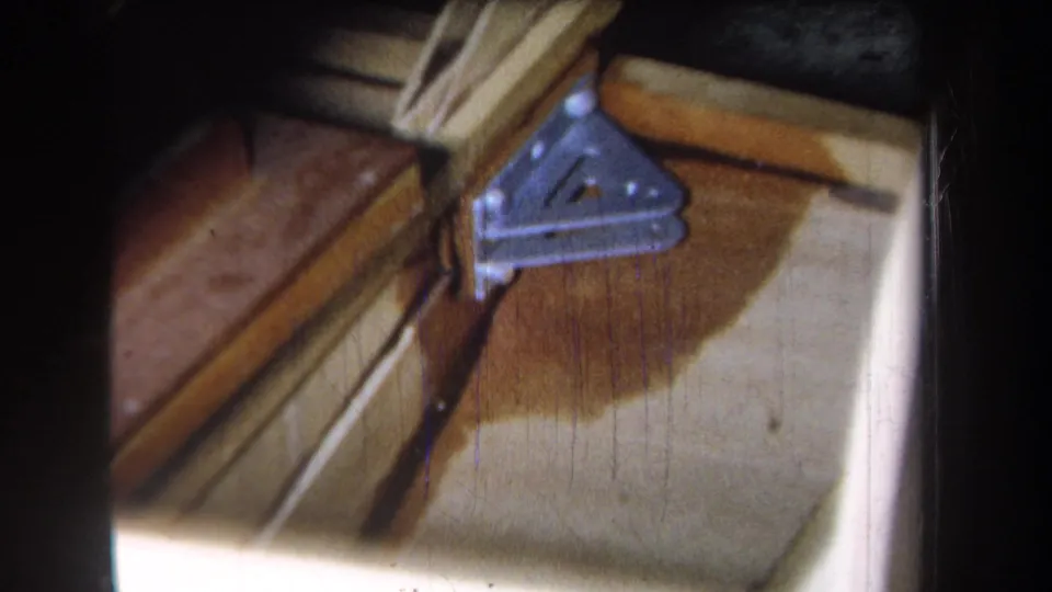 Close 8mm view from the 1965 Yucaipa reel of a metal bracket attached to wood, with staining and strong shadow across the surface.