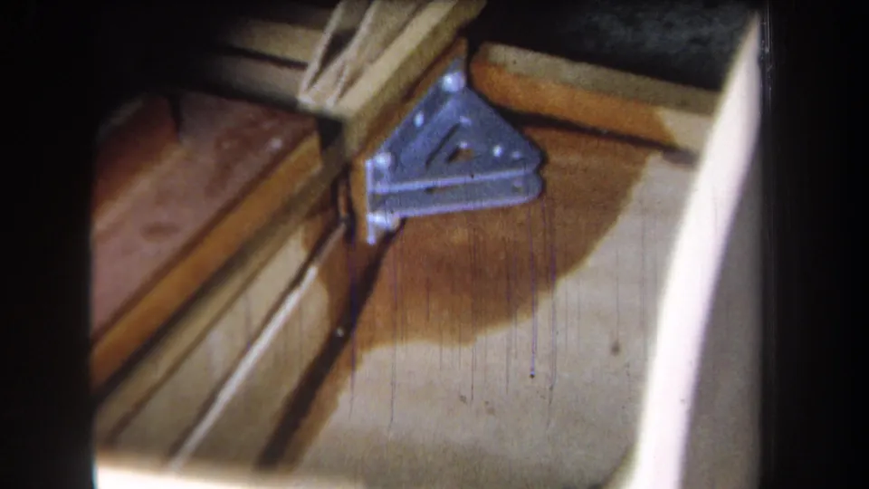 A slightly shifted 1965 8mm close-up shows the triangular brace, screw holes, exposed wood, and a broad dark stain below it.