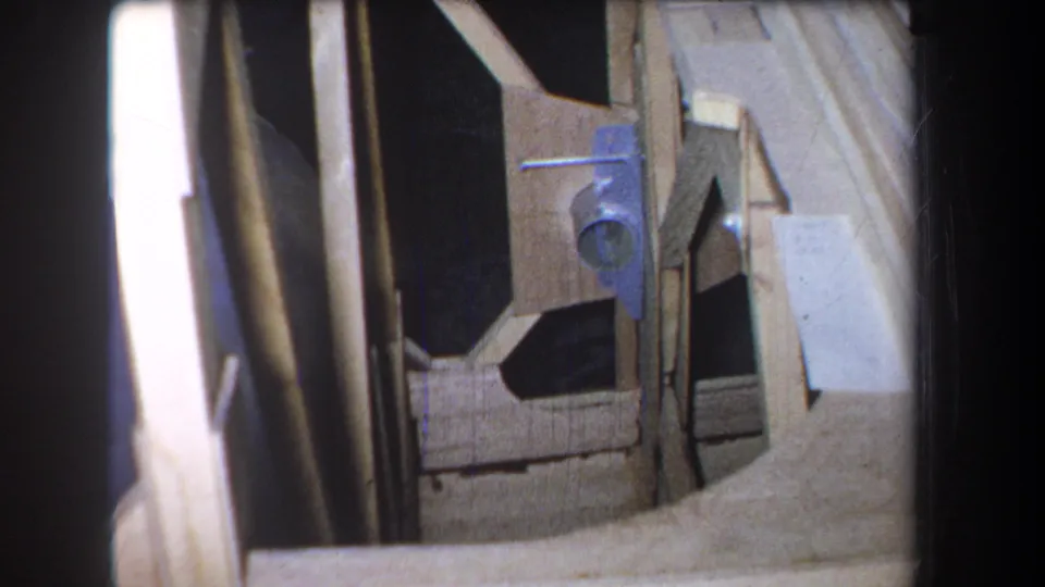 The final frame widens to show more wood framing around the blue-gray brace, with dark gaps, pale boards, and heavy shadow.