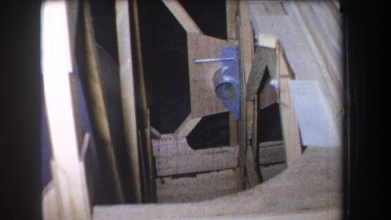 1965 8mm closeup from Volmer Yucaipa showing exposed wooden framing, joinery edges, pale boards, dark openings, and a small blue bracket.