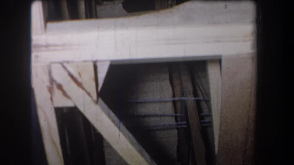 1965 8mm view in Volmer Yucaipa showing a horizontal plank, diagonal brace, vertical timber, and shadowed unfinished construction space.