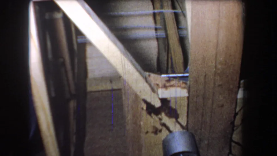 1965 Volmer Yucaipa closeup of exposed framing, showing diagonal pale lumber, a vertical post, dark cavity, stains, and a hanging cord or wire.