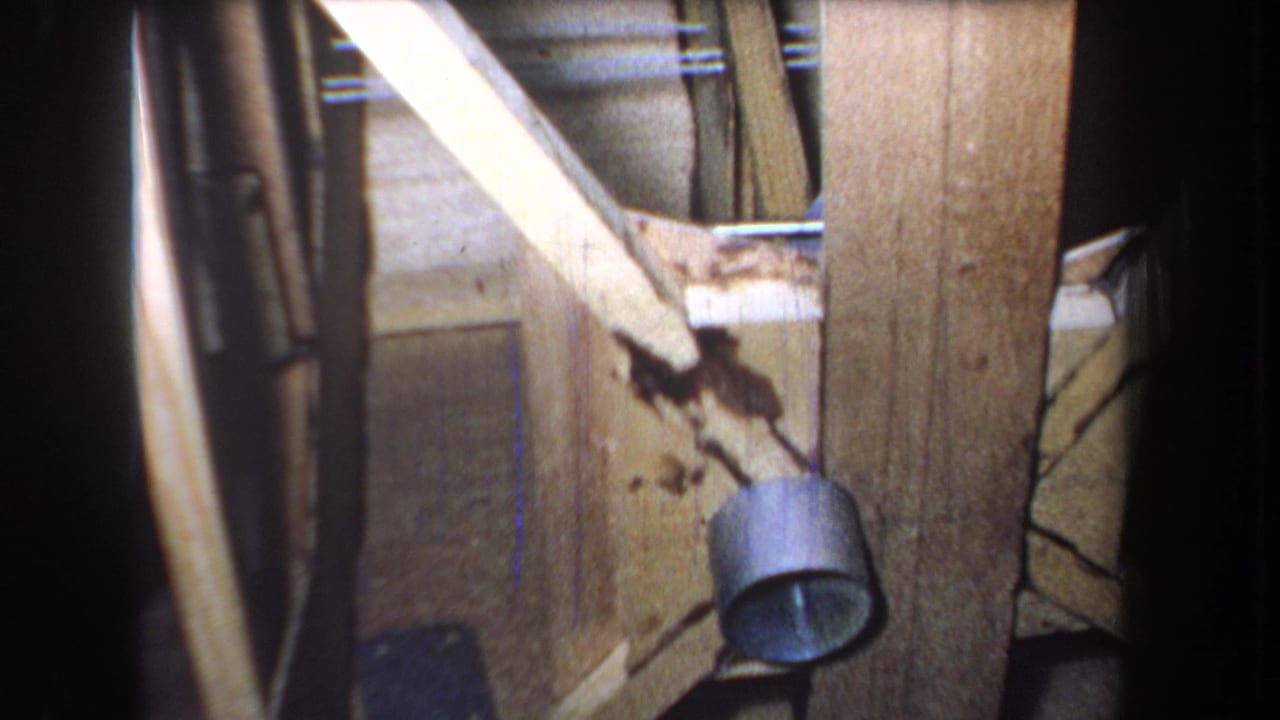 1965 Yucaipa-area 8mm frame showing aged wooden door boards, diagonal bracing, a round metal fixture, stains, and shadowed edges.