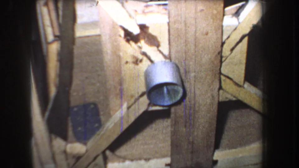 Final 1965 8mm frame holds on a worn wooden door, round metal fixture, diagonal brace, stains, cracks, and shadowed surrounding surfaces.