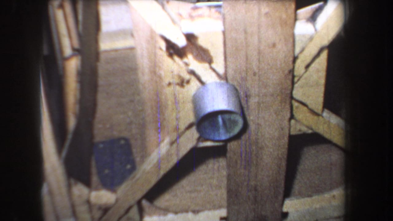 1965 8mm frame from Yucaipa-area footage showing a handmade wooden support with a small metal pulley component and dark film border.