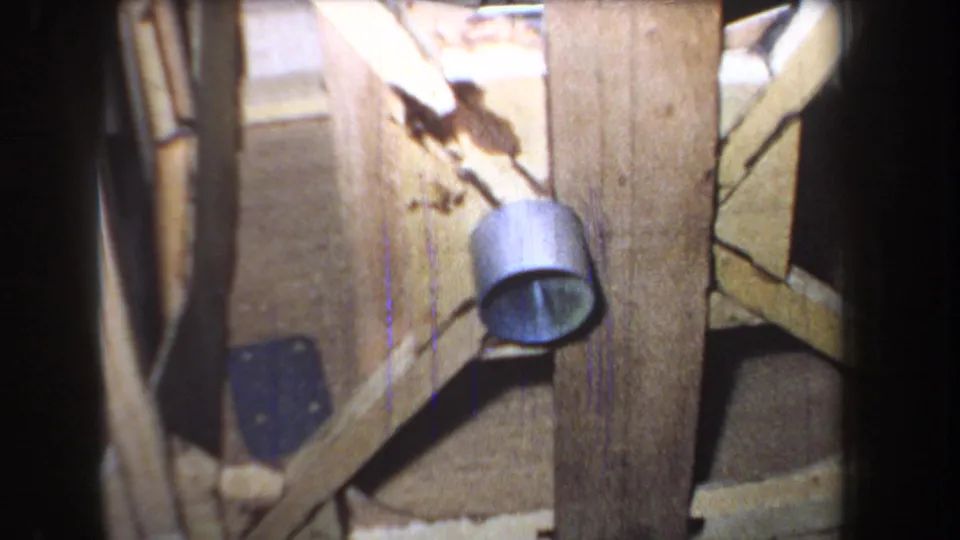 1965 8mm frame from Yucaipa-area footage showing a handmade wooden support with a small metal pulley component and dark film border.