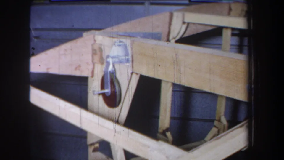 1965 8mm footage shows a pale wooden pulley framework with a metal wheel and bracket, likely in a workshop or utility setting near Yucaipa.