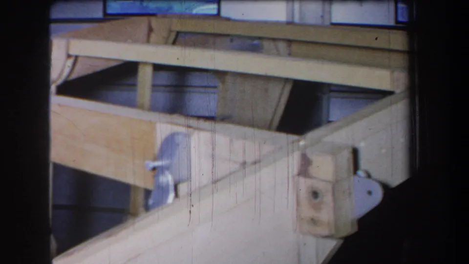 1965 Yucaipa home-movie frame showing pale wooden structural members, a diagonal brace, and metal fastening hardware.