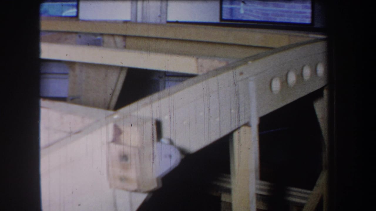 Wooden frame rail with circular holes and metal hardware near a vertical support.