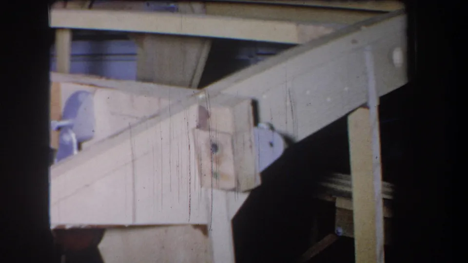 Close 8mm frame of the wooden mechanism in Yucaipa, with angled lumber, a metal bracket, and a shaded opening behind the structure.