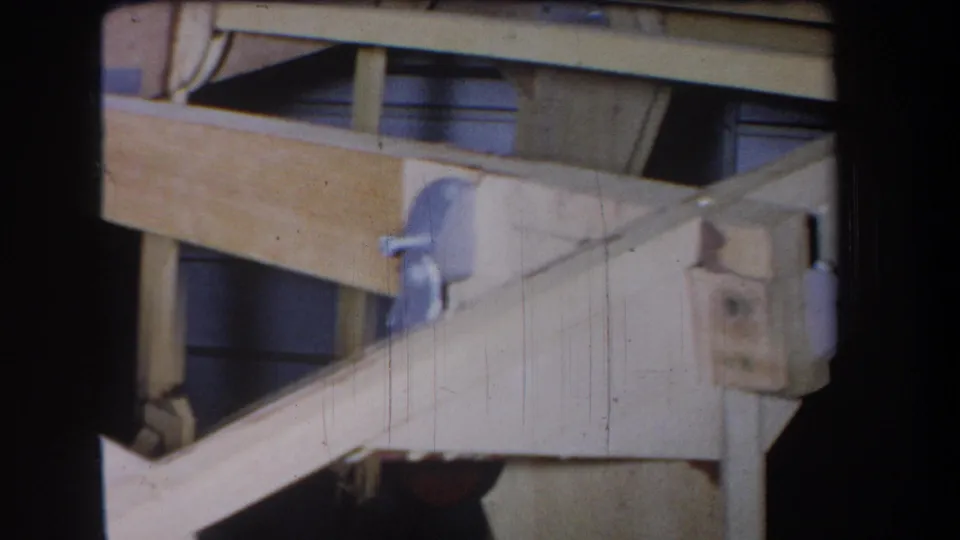 1965 8mm view of the wooden mechanical structure, showing layered beams, diagonal bracing, and a metal bracket at close range.