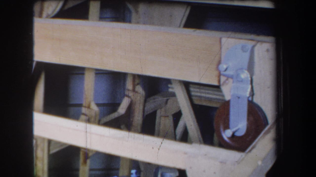 Wooden boards cross in front of a metal wheel and bracket assembly.