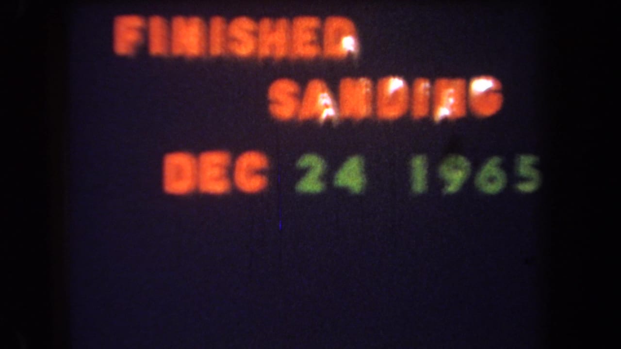 1965 8mm home-movie frame showing a projected card with orange FINISHED SANDING text and green DEC 24 1965 date.