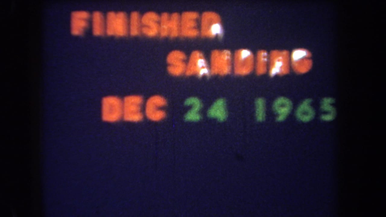 1965 8mm home-movie title text reads FINISHED SANDING DEC 24 1965 in orange and green on a dark blue field.