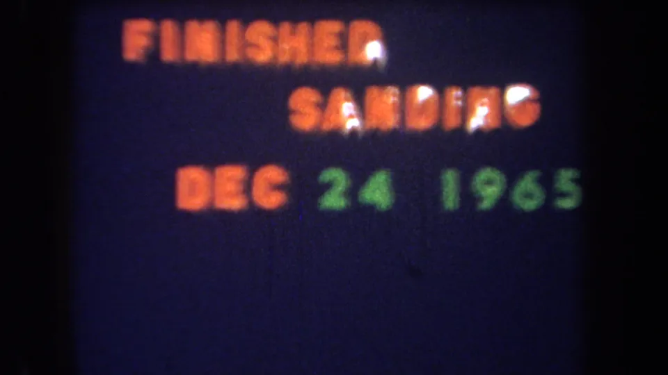 1965 8mm home-movie title text reads FINISHED SANDING DEC 24 1965 in orange and green on a dark blue field.