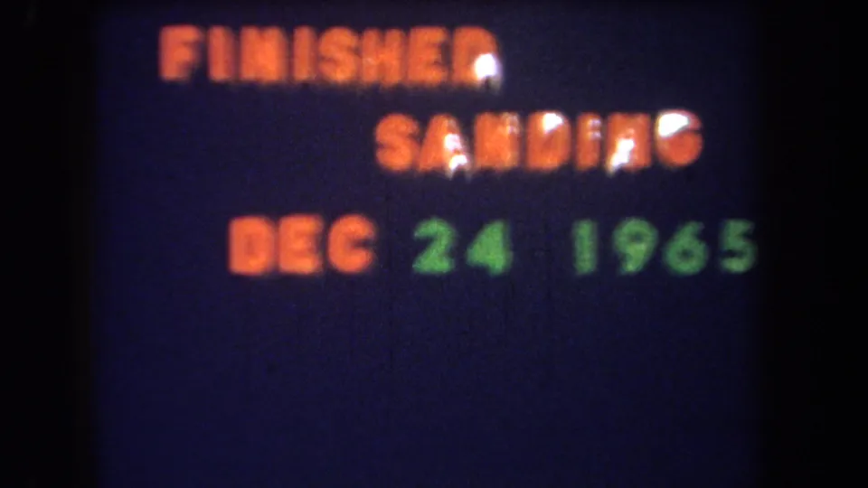 The same 1965 title card remains on screen, with orange project text and green date text softened by film blur.