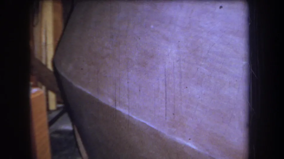 The camera holds on the curved sanded surface, with wood and shadowed workshop materials visible along the side of the 8mm frame.