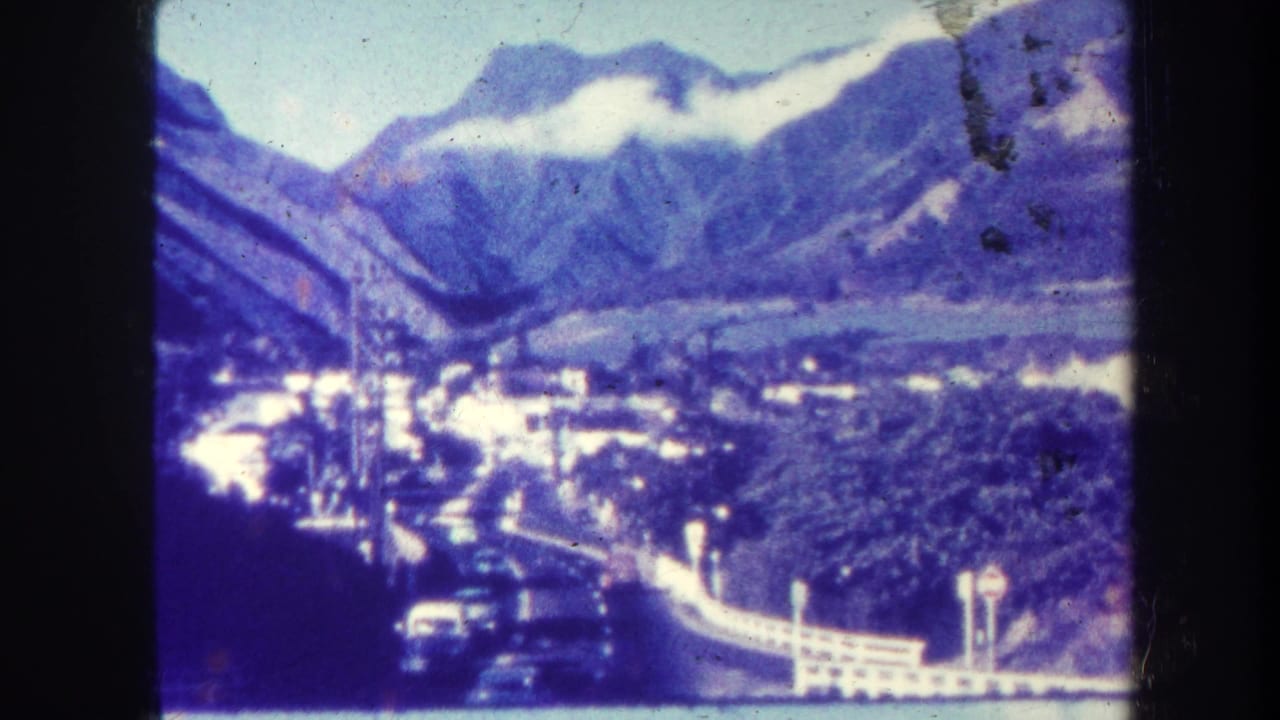 Elevated view of a valley road, cars, buildings, mountains, and low clouds.
