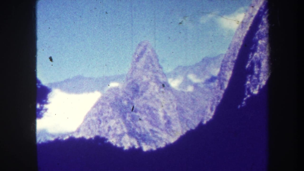 Pointed mountain peak with surrounding ridges, clouds, sky, and dark foreground edge.