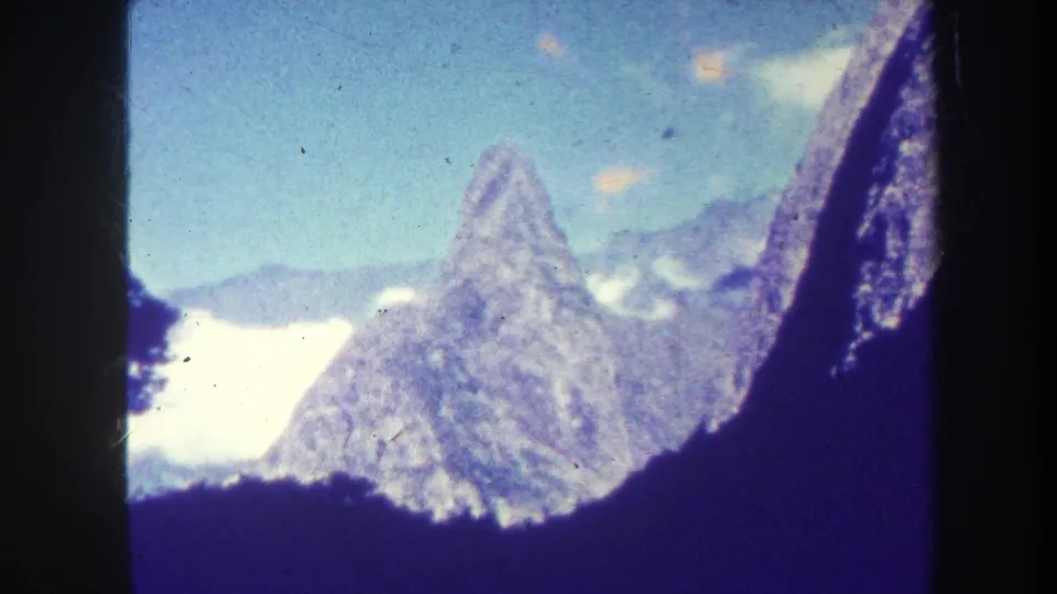 1967 Honolulu 8mm view of a mountain peak rising above a dark ridge, with clouds, sky, grain, and scratches visible.