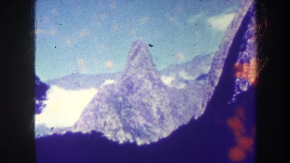 1967 Honolulu mountain view with a pointed peak, clouds, dark 8mm borders, and orange light leak along the right edge.