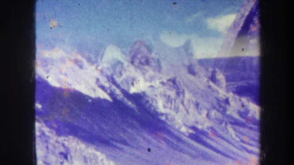 1967 8mm home-movie frame showing a snow-streaked ridge, distant pointed peak, blue sky, and soft film color shift.