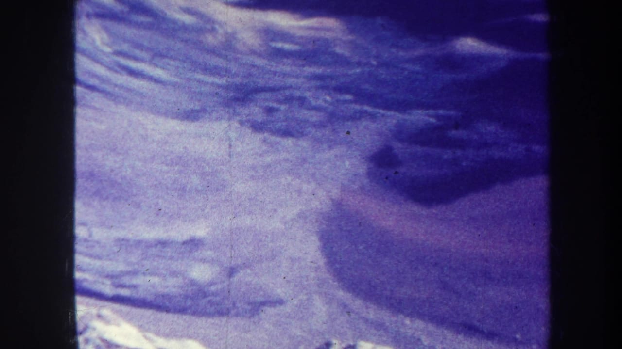 1967-attributed home-movie frame of a broad snowy hillside, dark ridge shadow, and soft exposure from aged 8mm film.