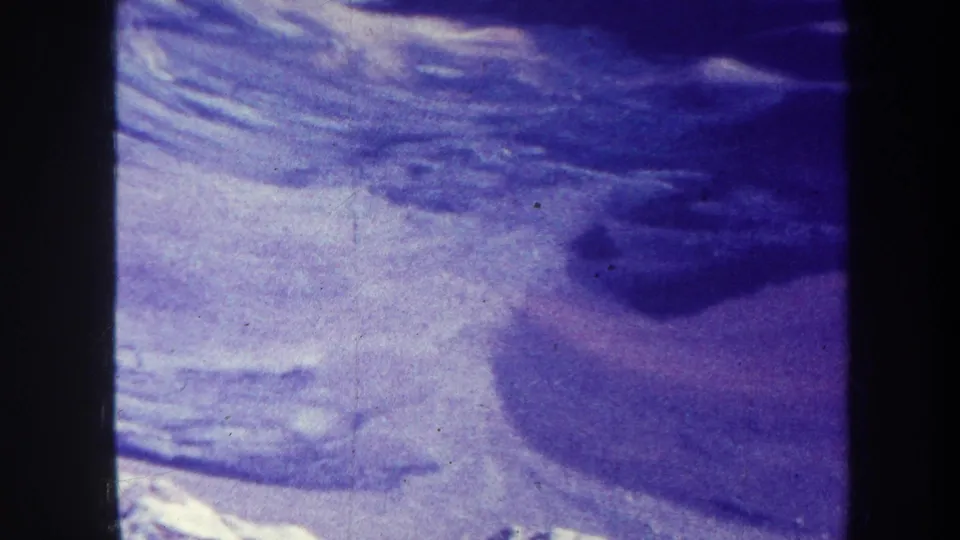 1967-attributed home-movie frame of a broad snowy hillside, dark ridge shadow, and soft exposure from aged 8mm film.