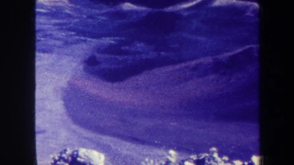 1967-attributed 8mm frame showing a dark mountain mass with surrounding snow patches and visible grain, dust, and soft focus.