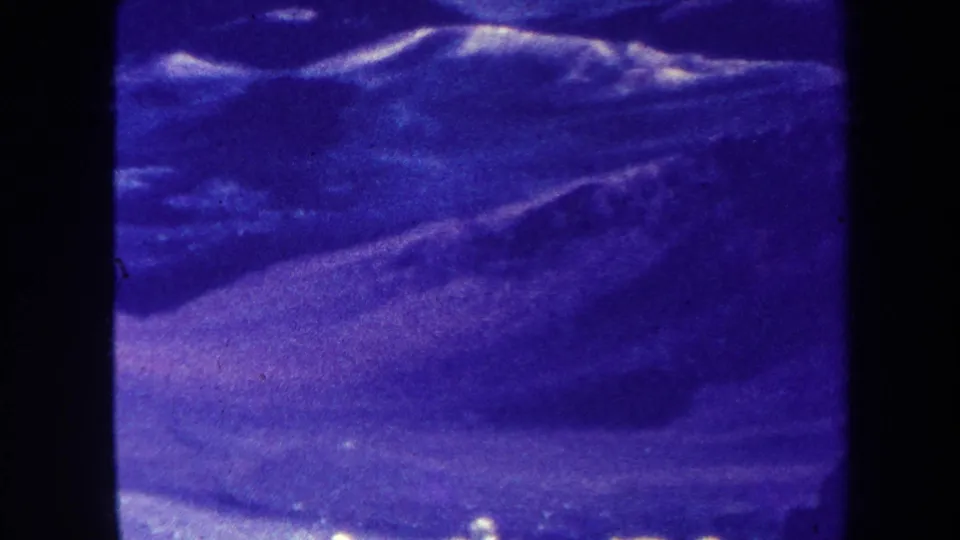 1967-attributed frame with a snowy ridge, dark hillside, and visible 8mm texture including dust, grain, and color fading.